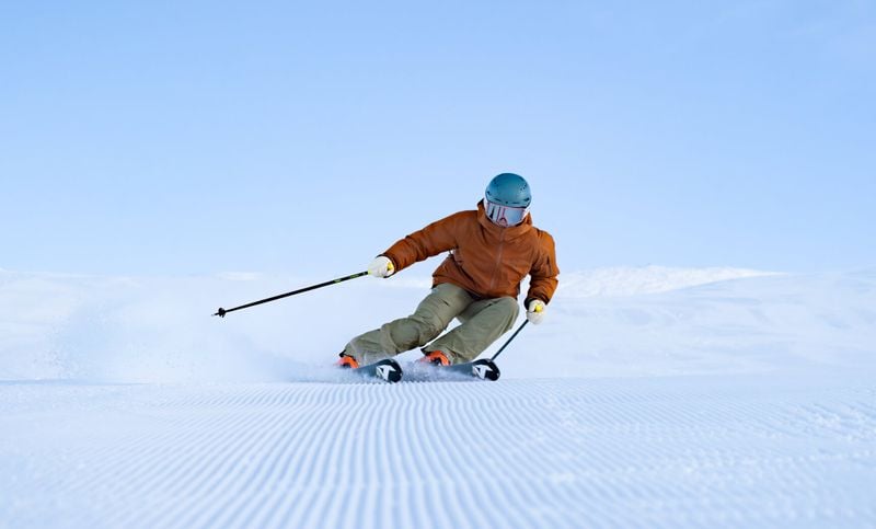 Person in an orange jacket,ski goggles & helmet, skiing down a freshly groomed mountain trail