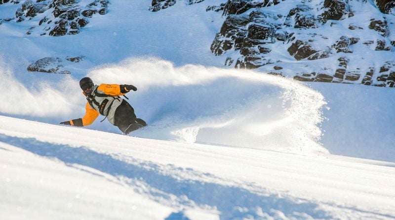Snowboarder carving through fresh powder snow on a steep alpine slope at Mt Hutt ski field