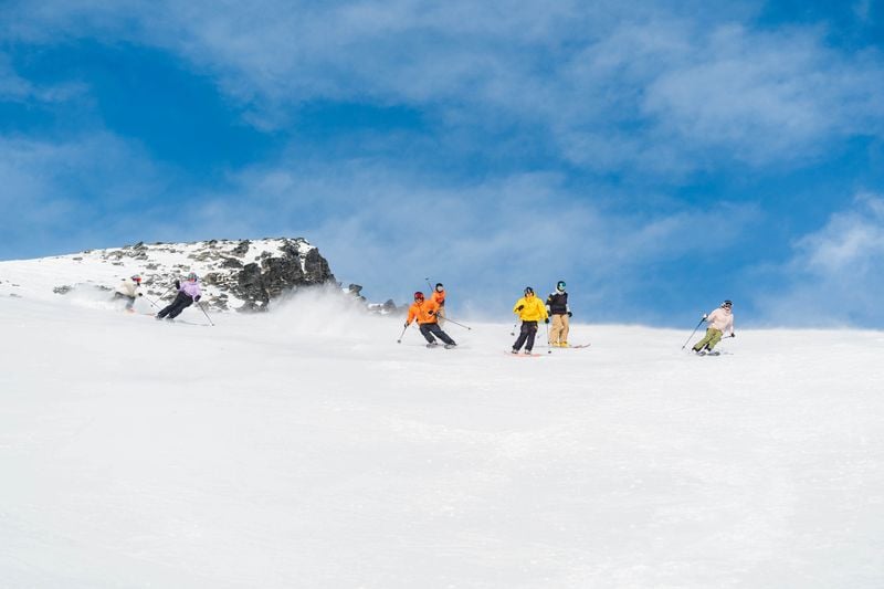 Group of skiers carving turns on a wide open slope at Mt Hutt ski field under a clear blue sky