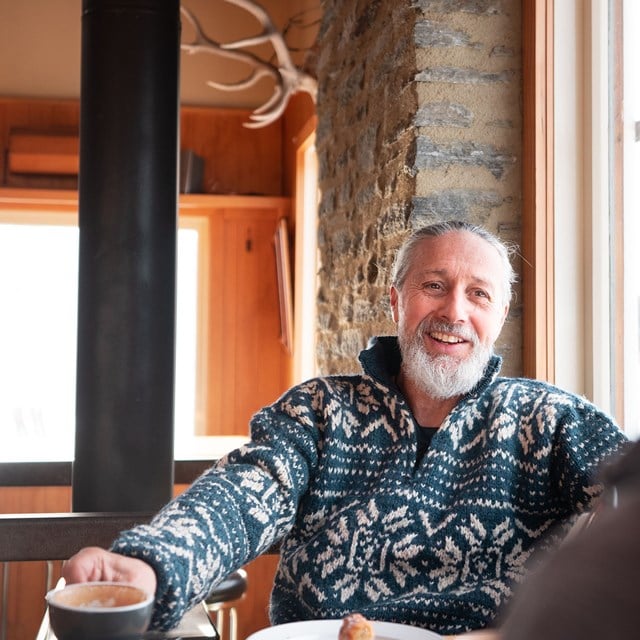 Man sitting in a chelet smiling with a coffee in hand.