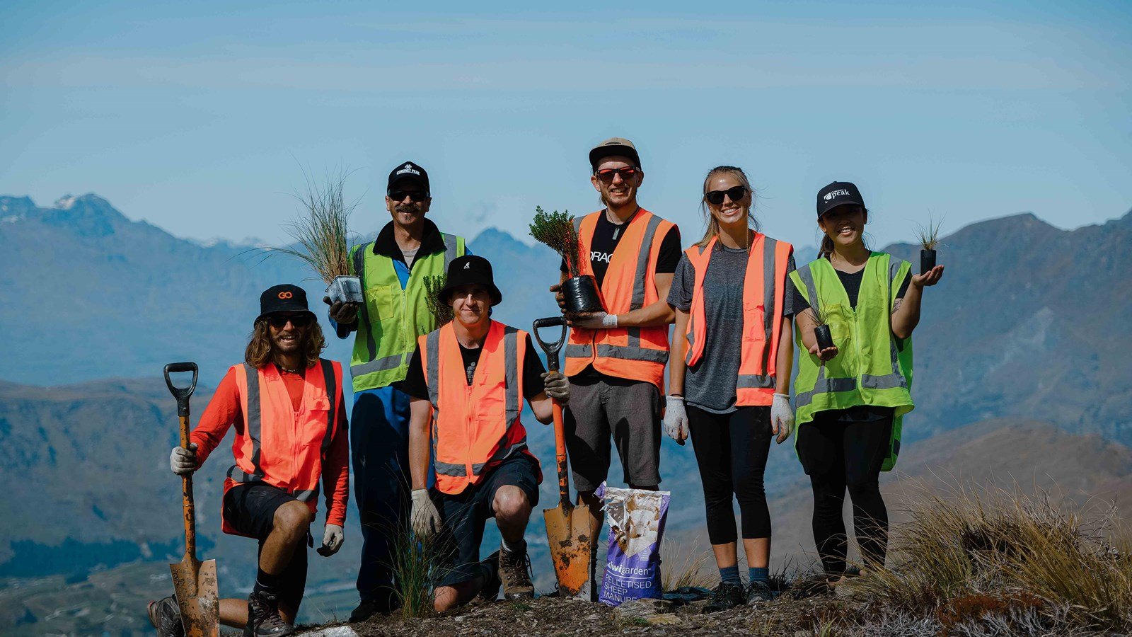 Group wearing high-vis vests smiling holding plants and shovels.