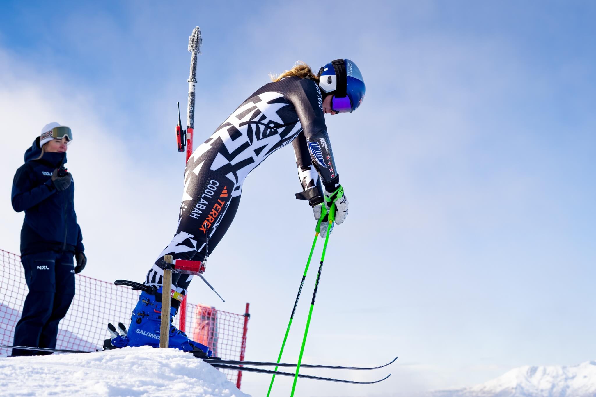 Skier in black and white suit leaning forward at start line ready to race on snowy slope.