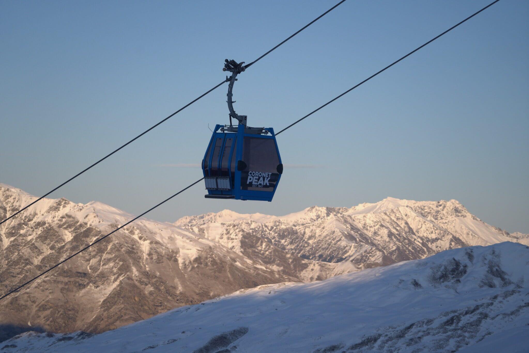 Blue Coronet Peak gondola cabin suspended over snowy mountain landscape at sunset.