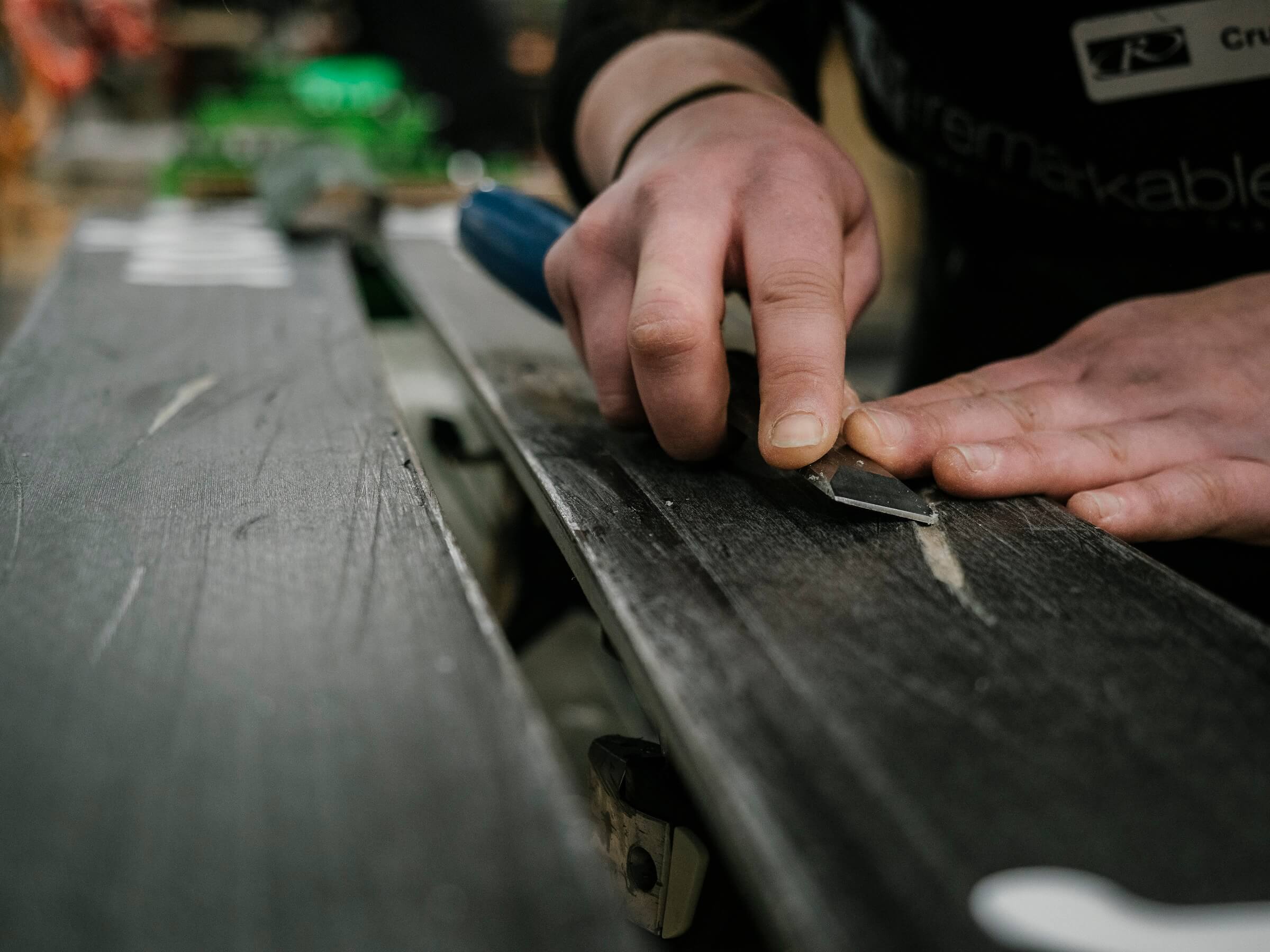 Person sharpening or scraping the base of a ski with a hand tool on a workbench.