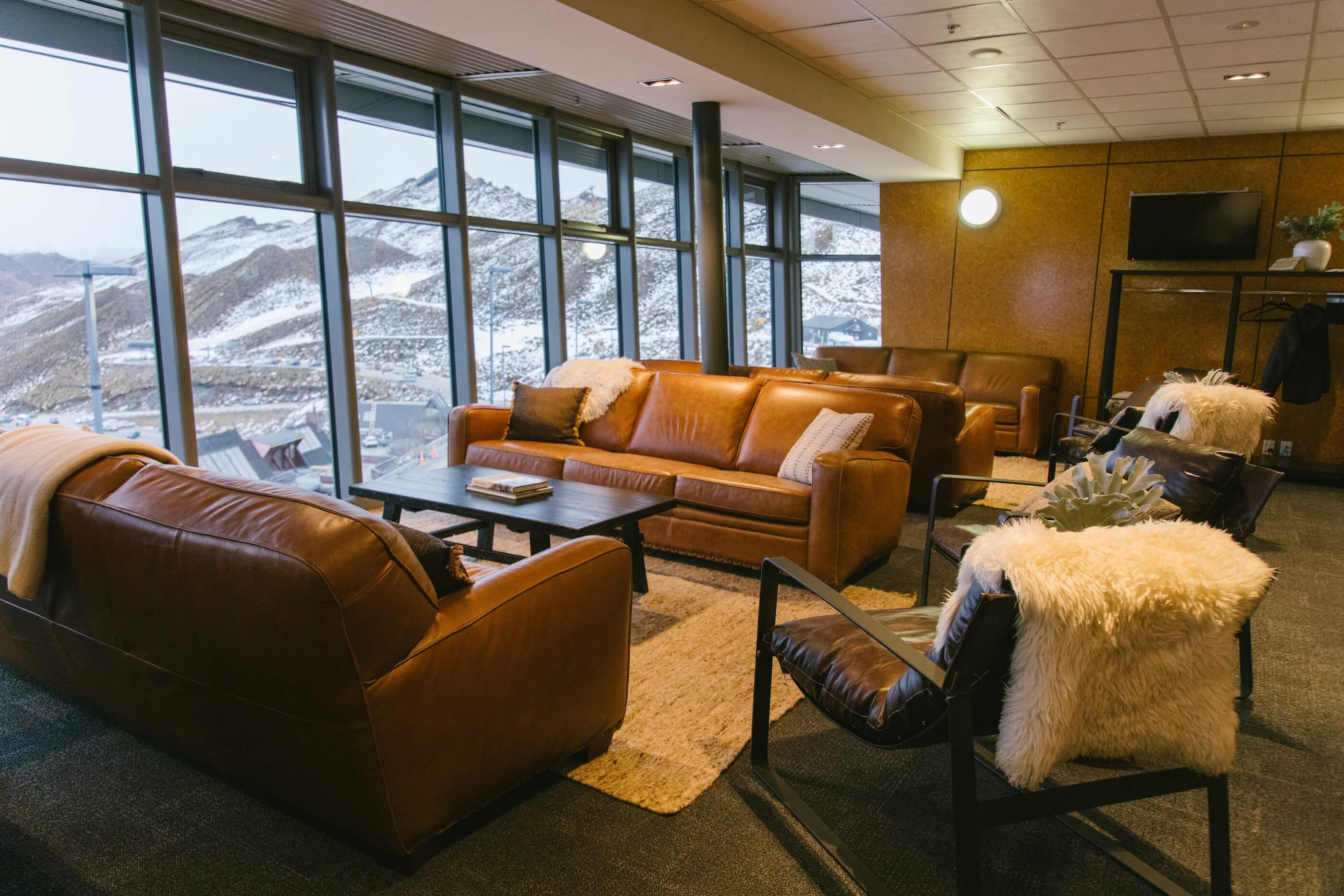 Cozy lounge with leather sofas and chairs overlooking snowy mountain peaks through large windows.