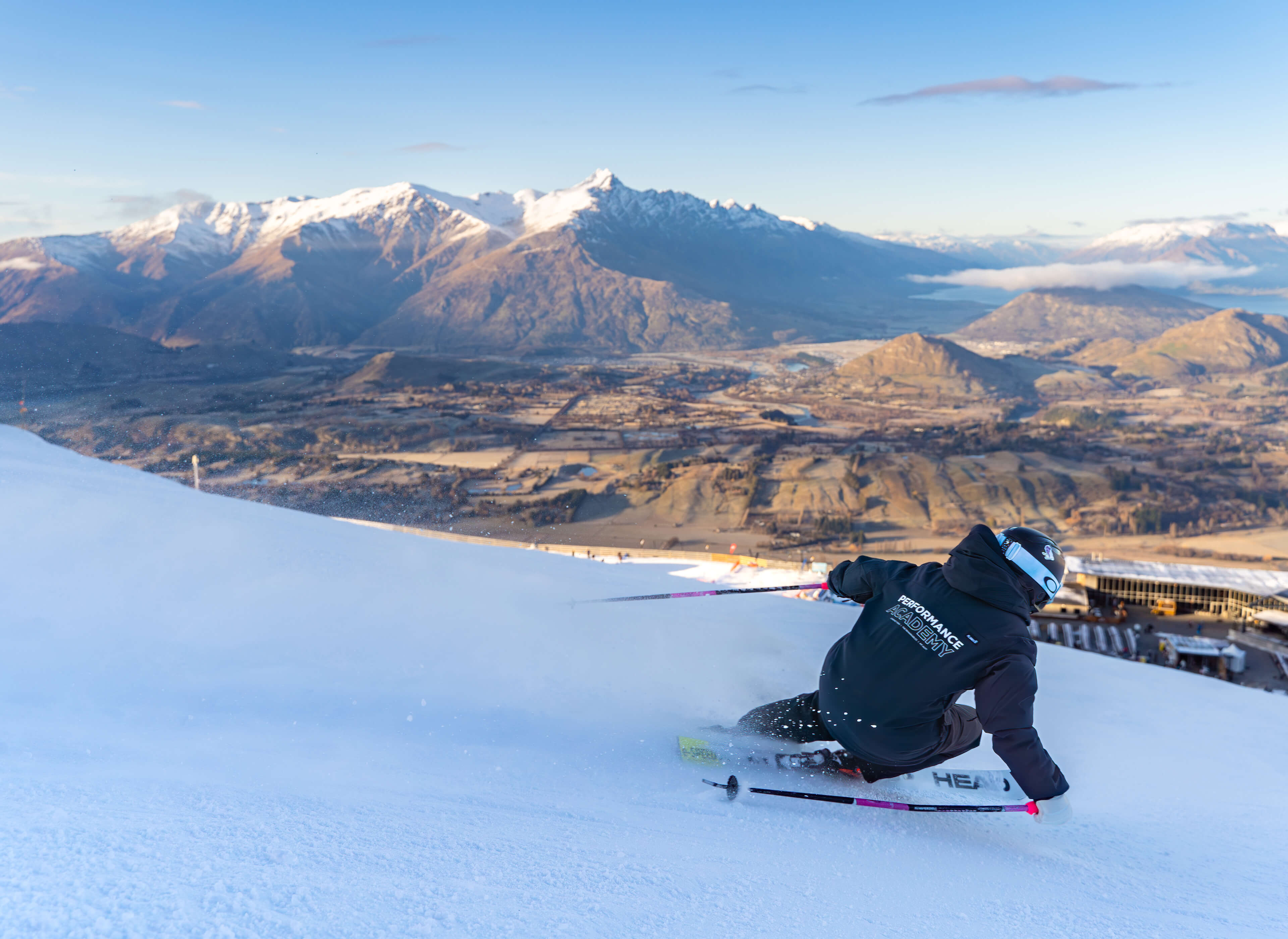 Skier carving down a snowy slope with mountains and valley in the background.