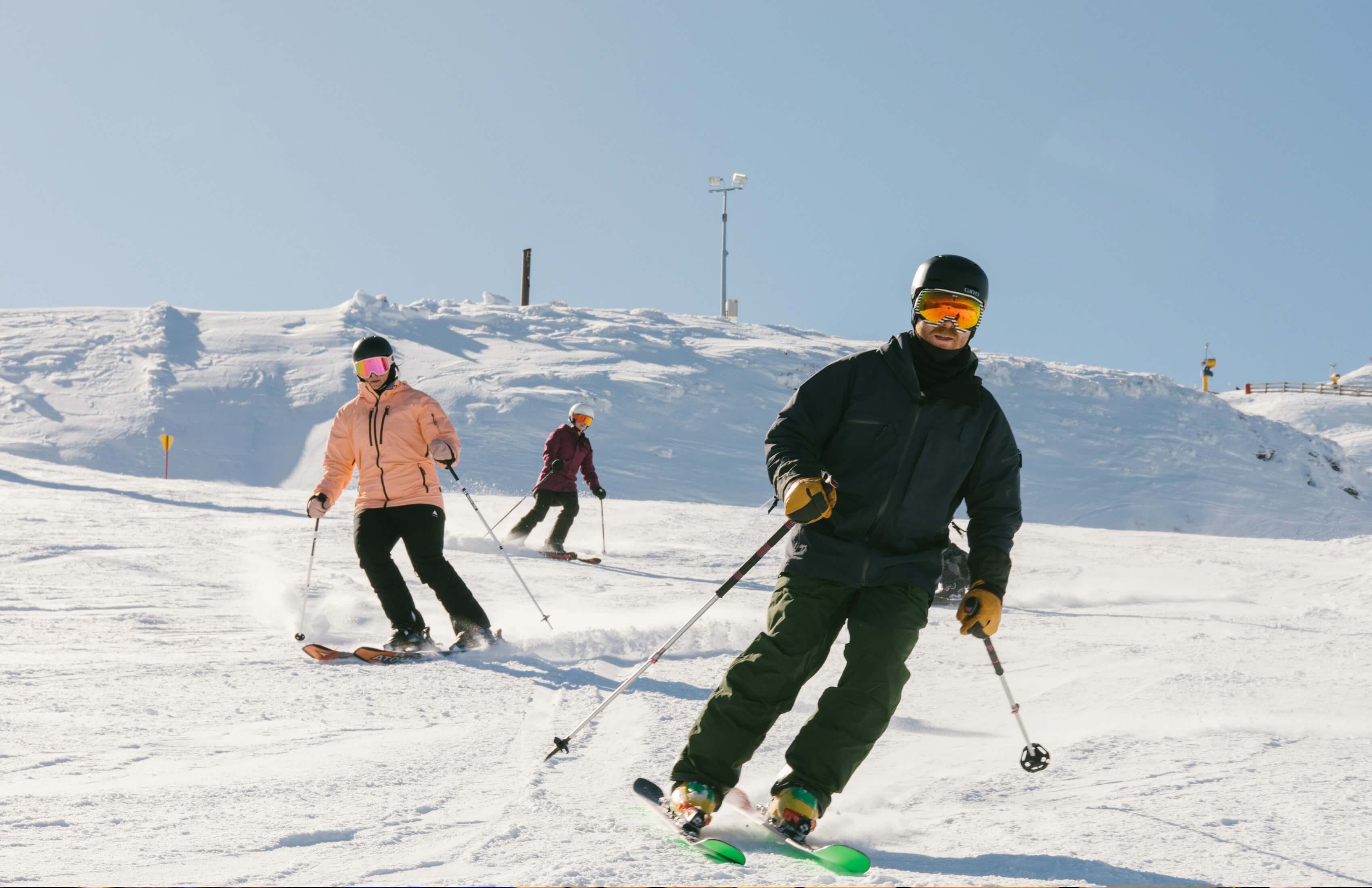 Three skiers wearing helmets and goggles skiing downhill on a snowy mountain under clear sky.