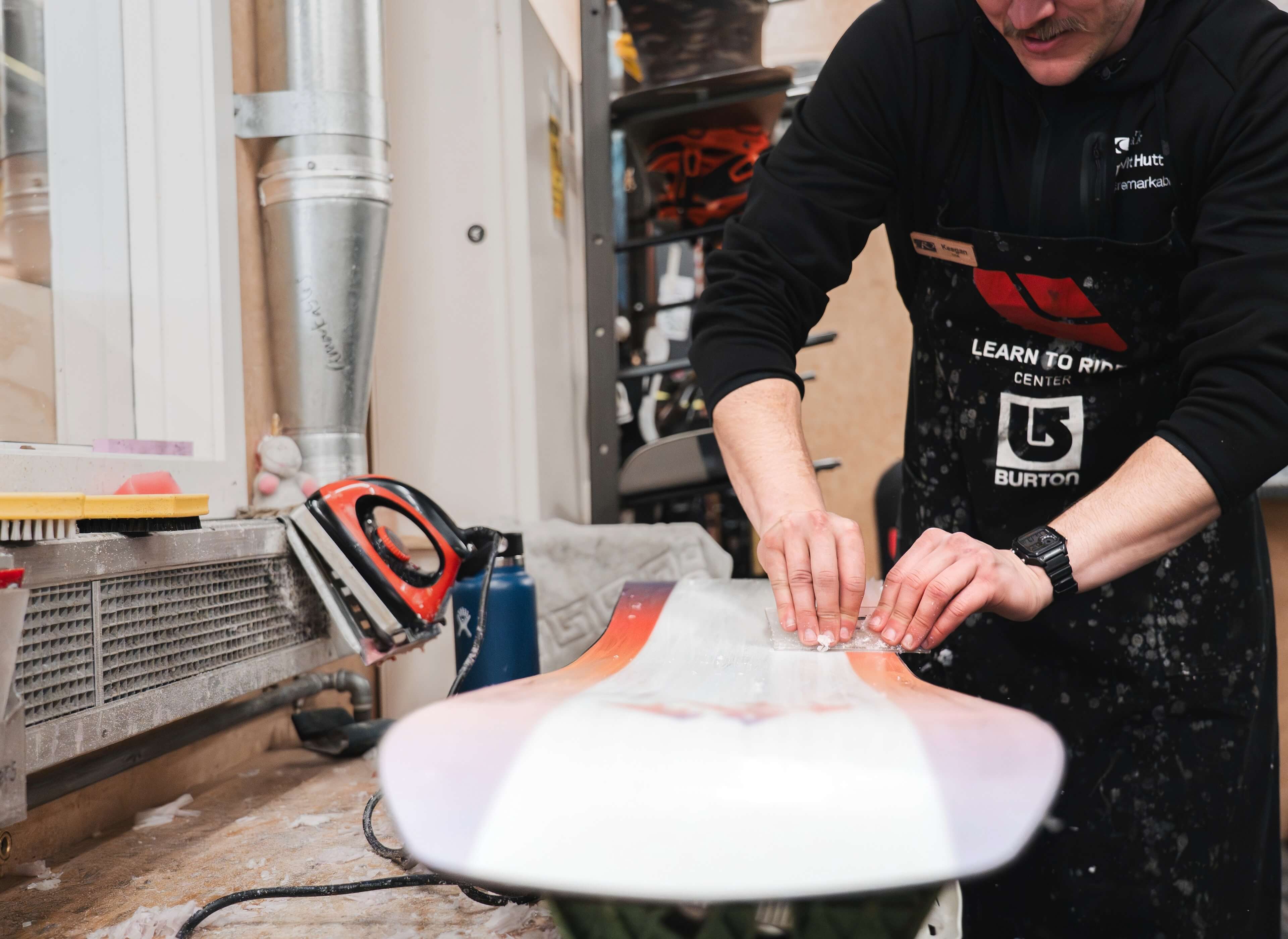 Person waxing a snowboard on a workbench inside a workshop.
