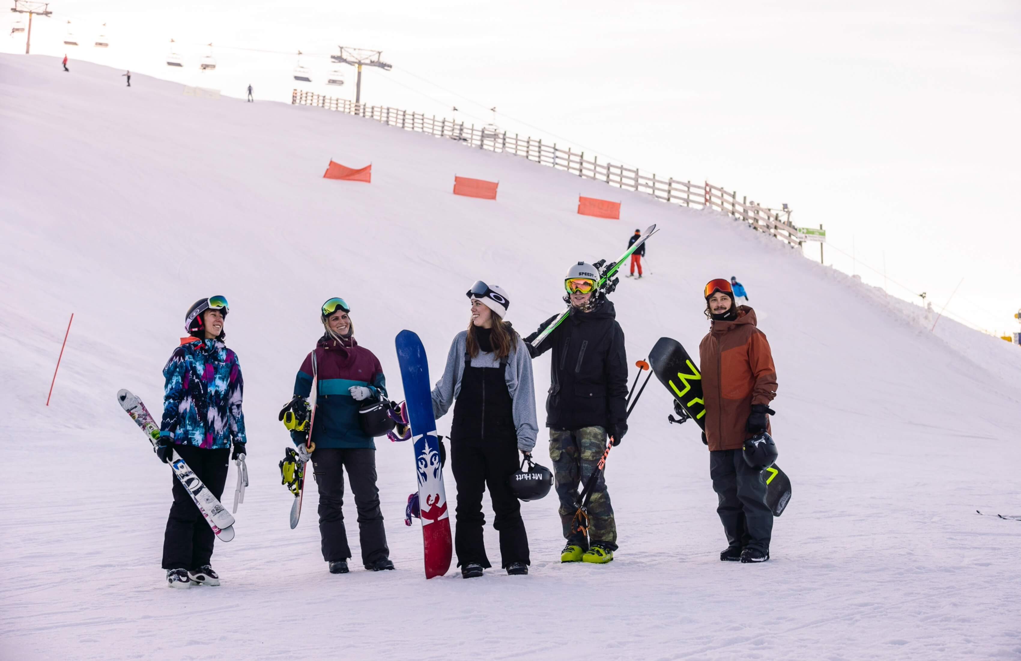 Group of five skiers and snowboarders standing on snowy slope at ski resort with chairlifts behind.