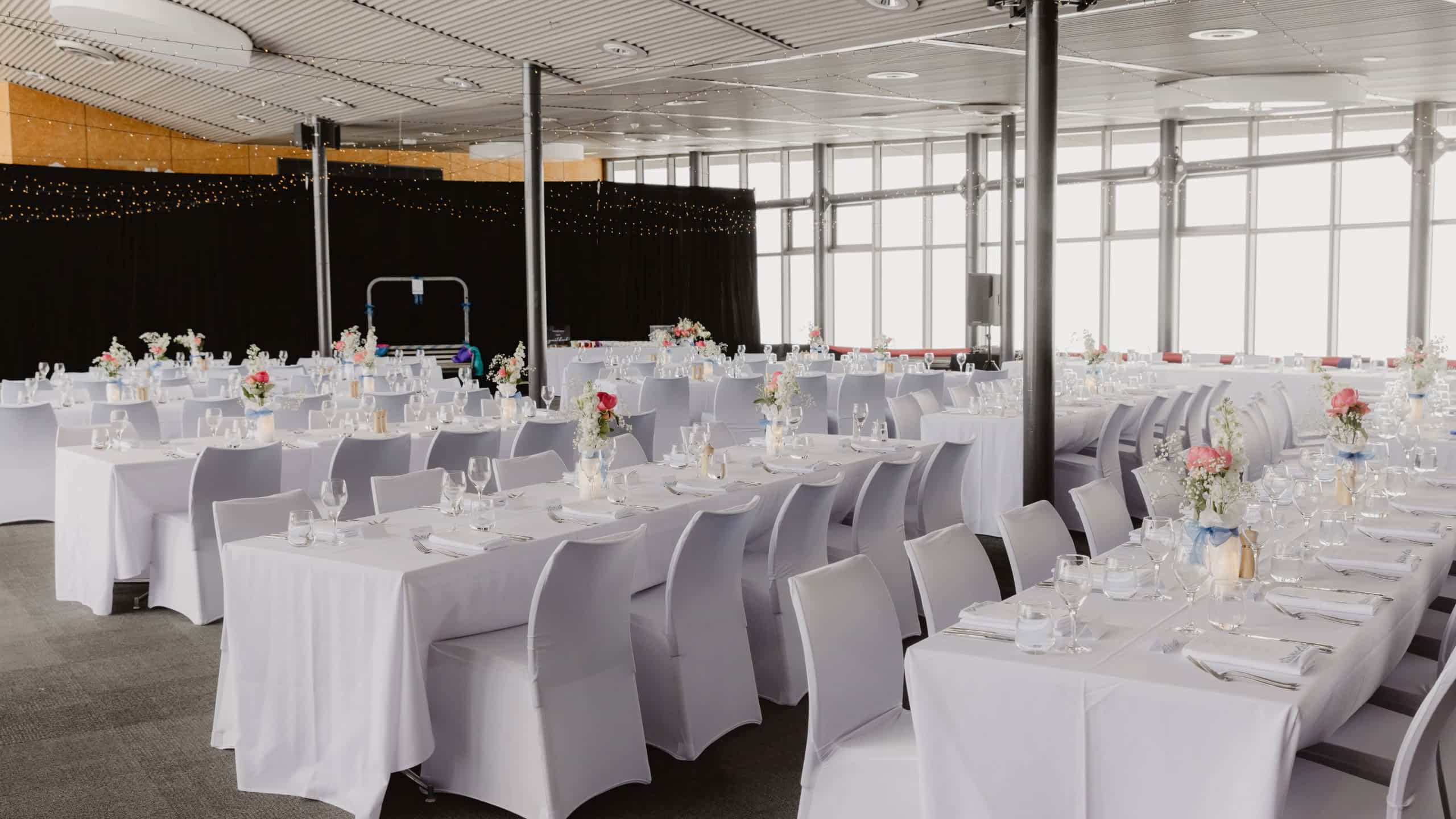 Large banquet hall with white tables and chairs set for an event with floral centerpieces.